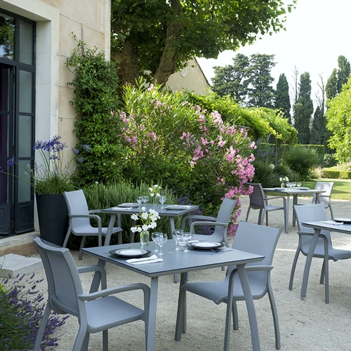 Mesas cuadradas Sunste con sus sillas apilables al exterior en un jardín francés